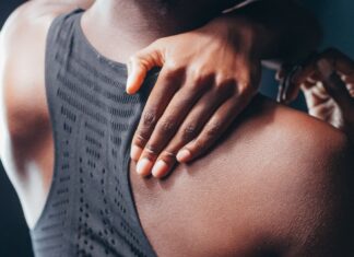 Ból barku po treningu: przyczyny, domowe testy i kiedy zgłosić się do fizjoterapeuty Osoba w sportowym biustonoszu trzyma bolący bark po treningu