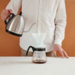 Osoba parząca kawę metodą przelewową z dripperem i czajnikiem